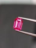 Pink gemstone held by tweezers against a blurred background