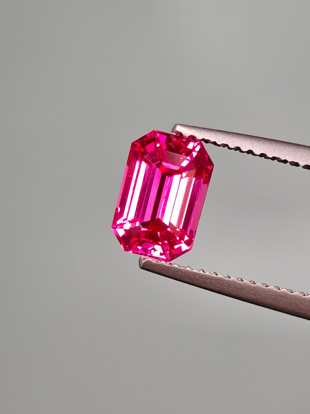 Pink gemstone held by tweezers against a gray background