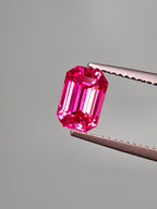 Pink gemstone held by tweezers against a gray background
