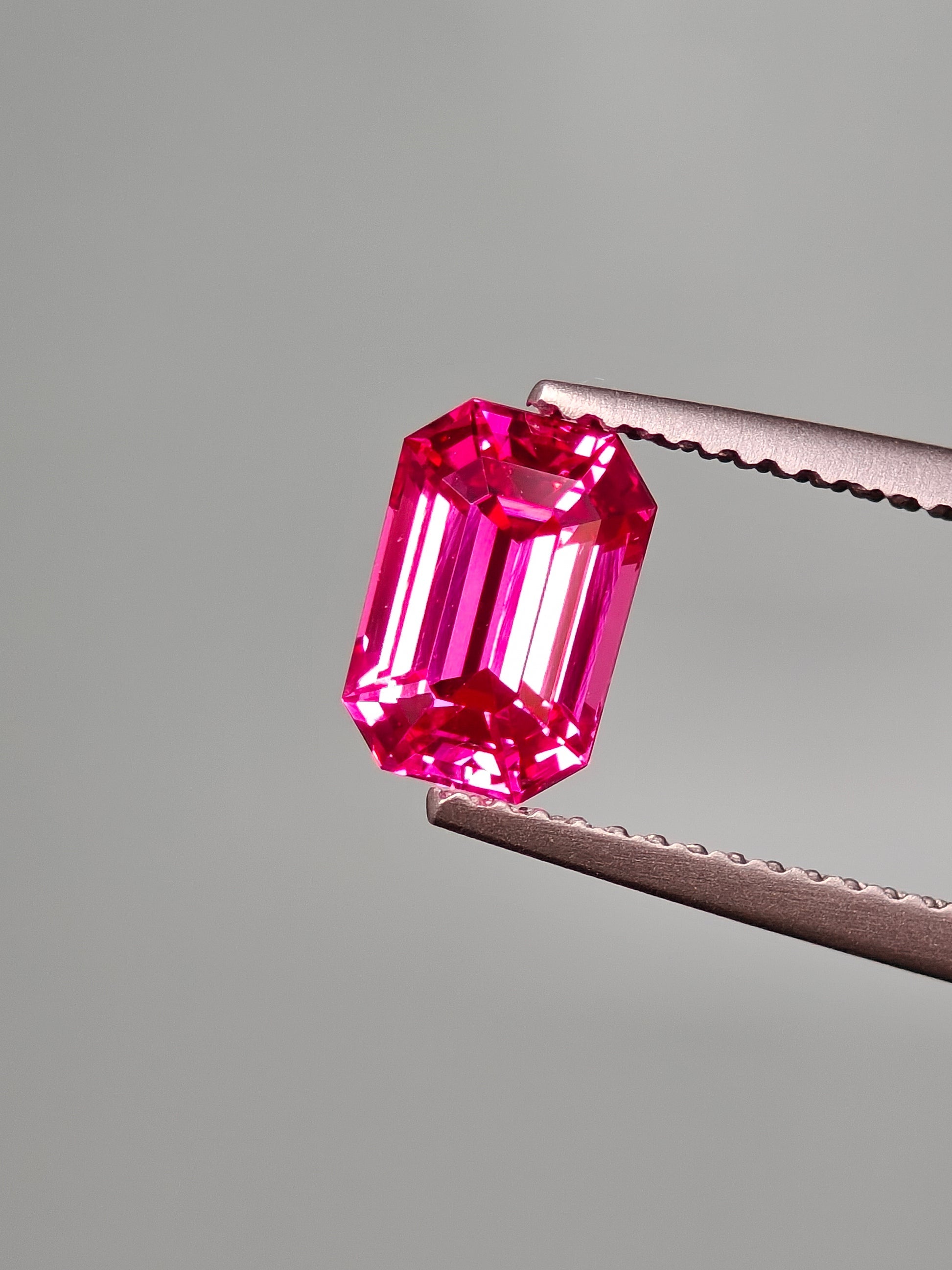 Pink gemstone held by tweezers against a gray background
