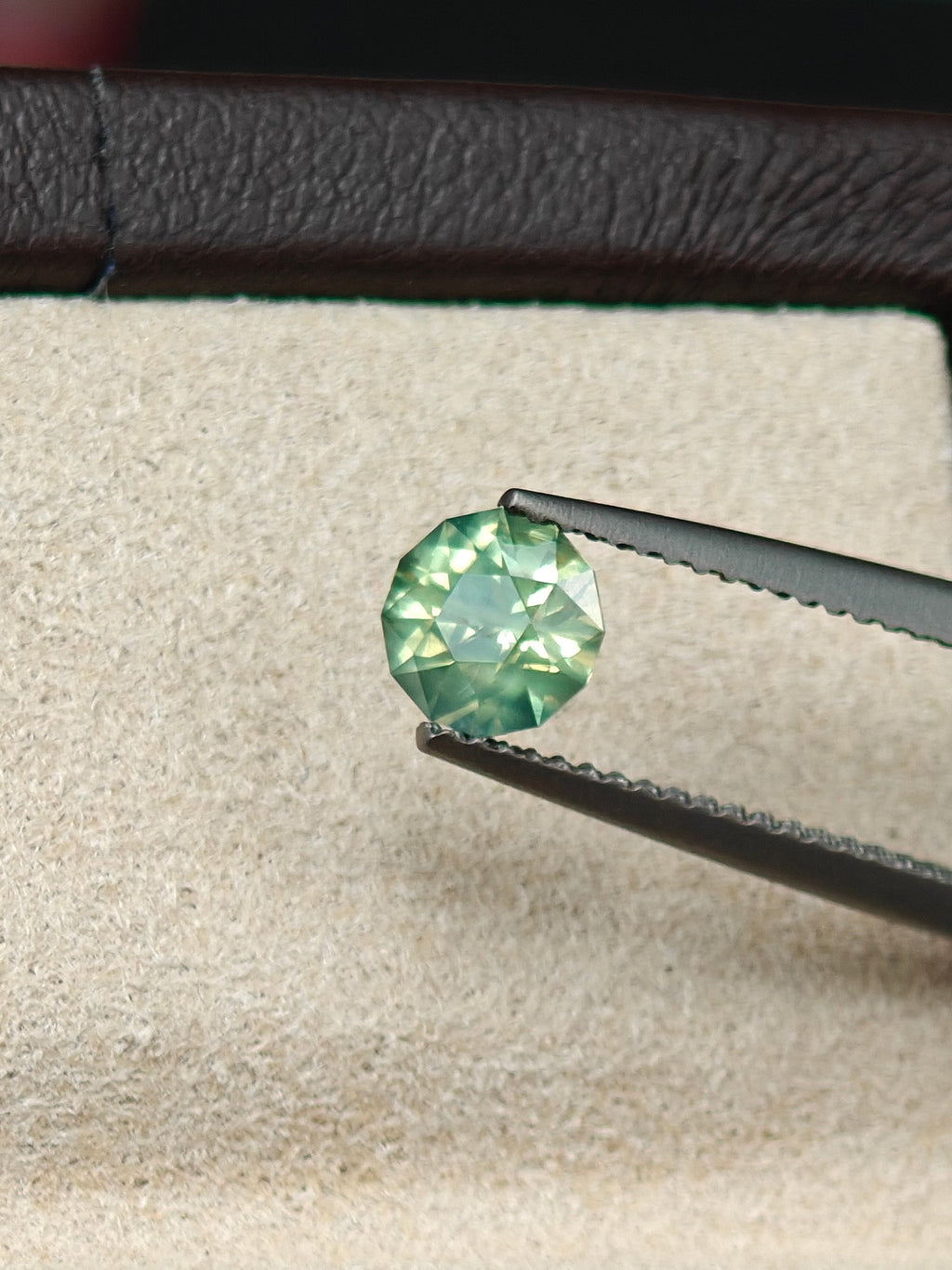 Green gemstone held by tweezers on a white cloth with a dark border