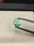 Green gemstone held by tweezers on a white cloth with a dark border