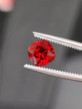 Red gemstone held by tweezers against a dark background