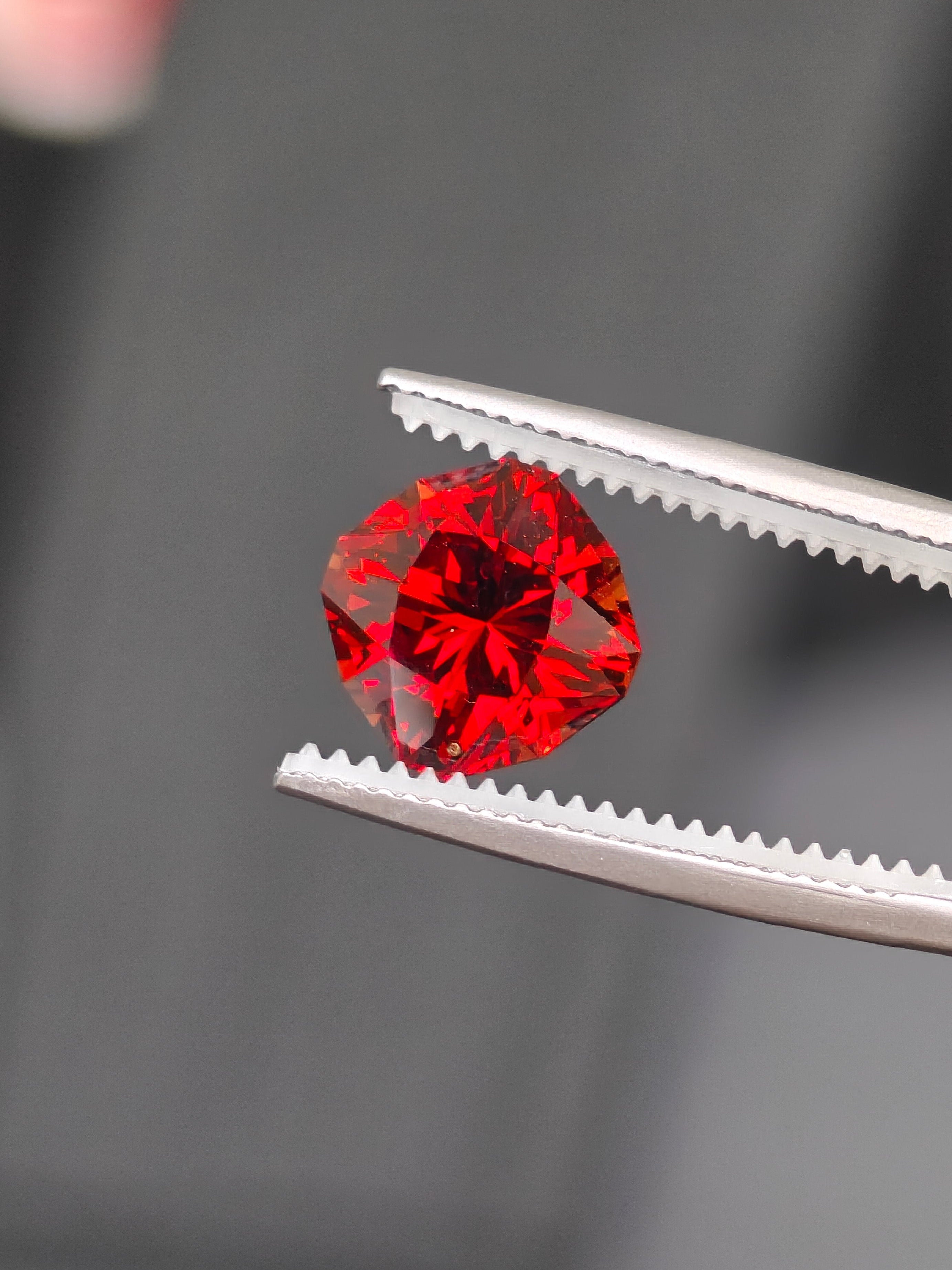 Red gemstone held by tweezers against a dark background
